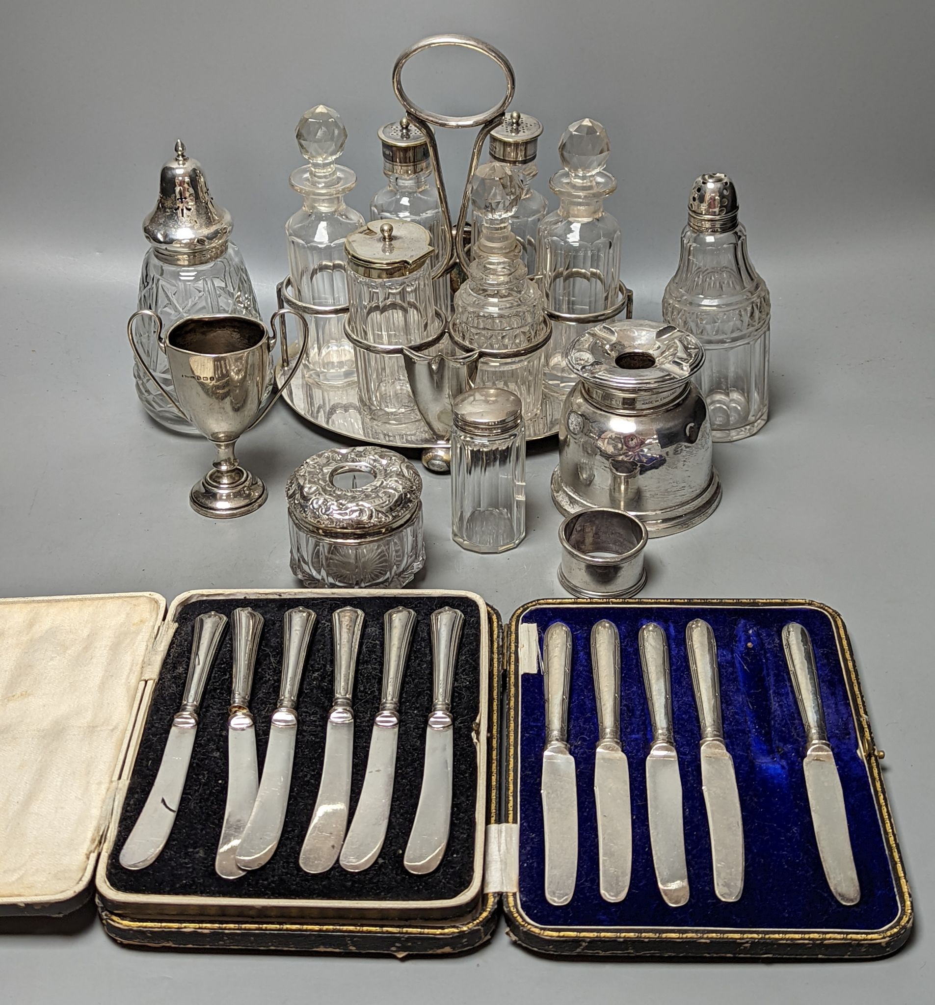 A plated cruet stand, two cased sets of silver handled tea knives, a silver domed ashtray(a.f.) silver trophy cup, four silver mounted glass jars and a plated napkin ring.